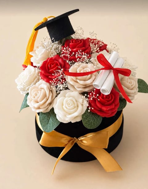 Graduation flower arrangement with red and cream roses, babys breath, diploma scroll, mortarboard cap, and gold ribbon in black hat box