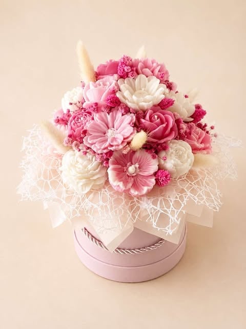 Pink and white flower arrangement in a round pink box with lace netting and decorative horn accents