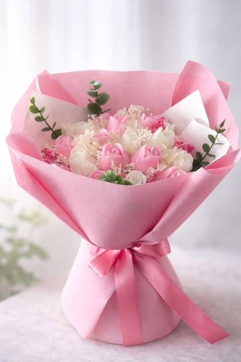 Pink and white flower bouquet wrapped in pink paper with a pink ribbon bow and green foliage accents