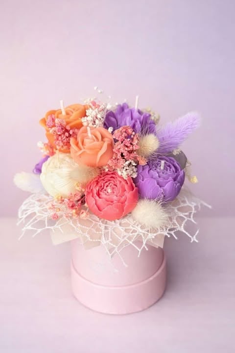 Colorful flower arrangement in a pink box featuring orange, pink, and purple roses with babys breath and dried grasses on pastel background