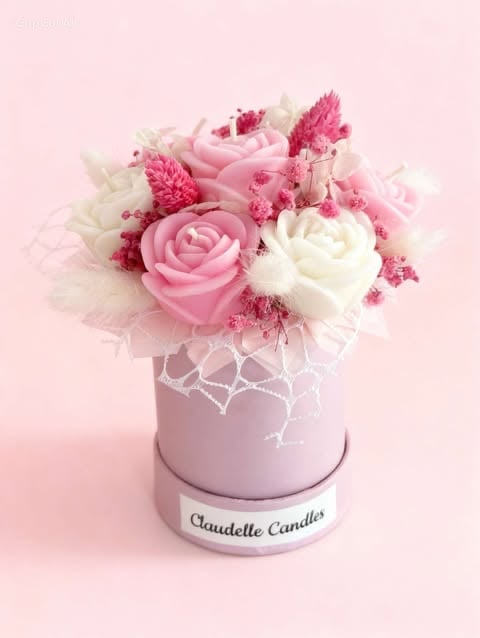 Pink and white roses with filler flowers arranged in a pale pink cylindrical Claudelle Candles box on a pink background