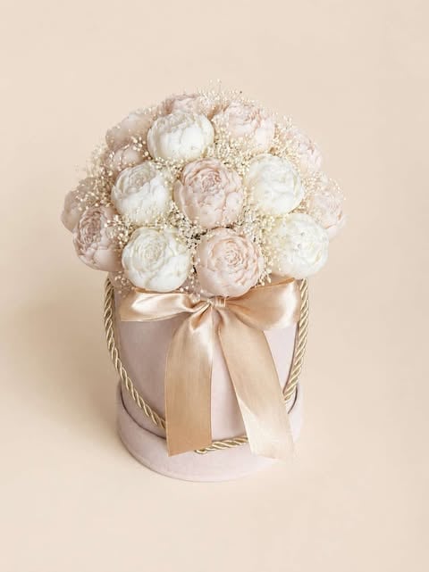 Elegant floral arrangement with white and blush peonies and babys breath in a cylindrical beige box tied with a satin bow