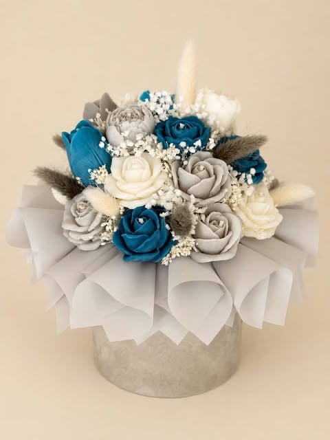 Elegant floral arrangement with blue, white, and gray roses with babys breath in a white textured vase with ribbon
