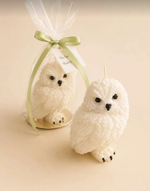 Two white fluffy decorative owl figurines with black beads for eyes and feet, one packaged in clear cellophane with a green ribbon bow