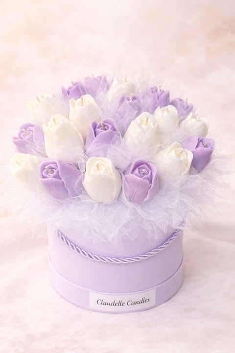 Lavender and white decorative rose arrangement in a round box labeled Claudelle Candles with tulle wrapping