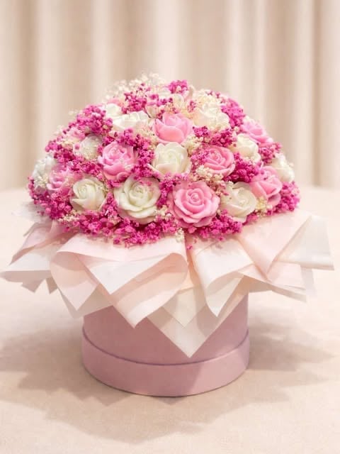 Elegant floral arrangement with pink and white roses and carnations in a pink hat box with ribbons