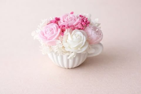 Pink and white artificial floral arrangement in a white ceramic pot against a light pink background