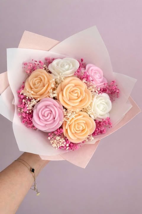 Hand holding a bouquet of peach, pink, and white roses with babys breath and magenta filler flowers wrapped in white tissue paper